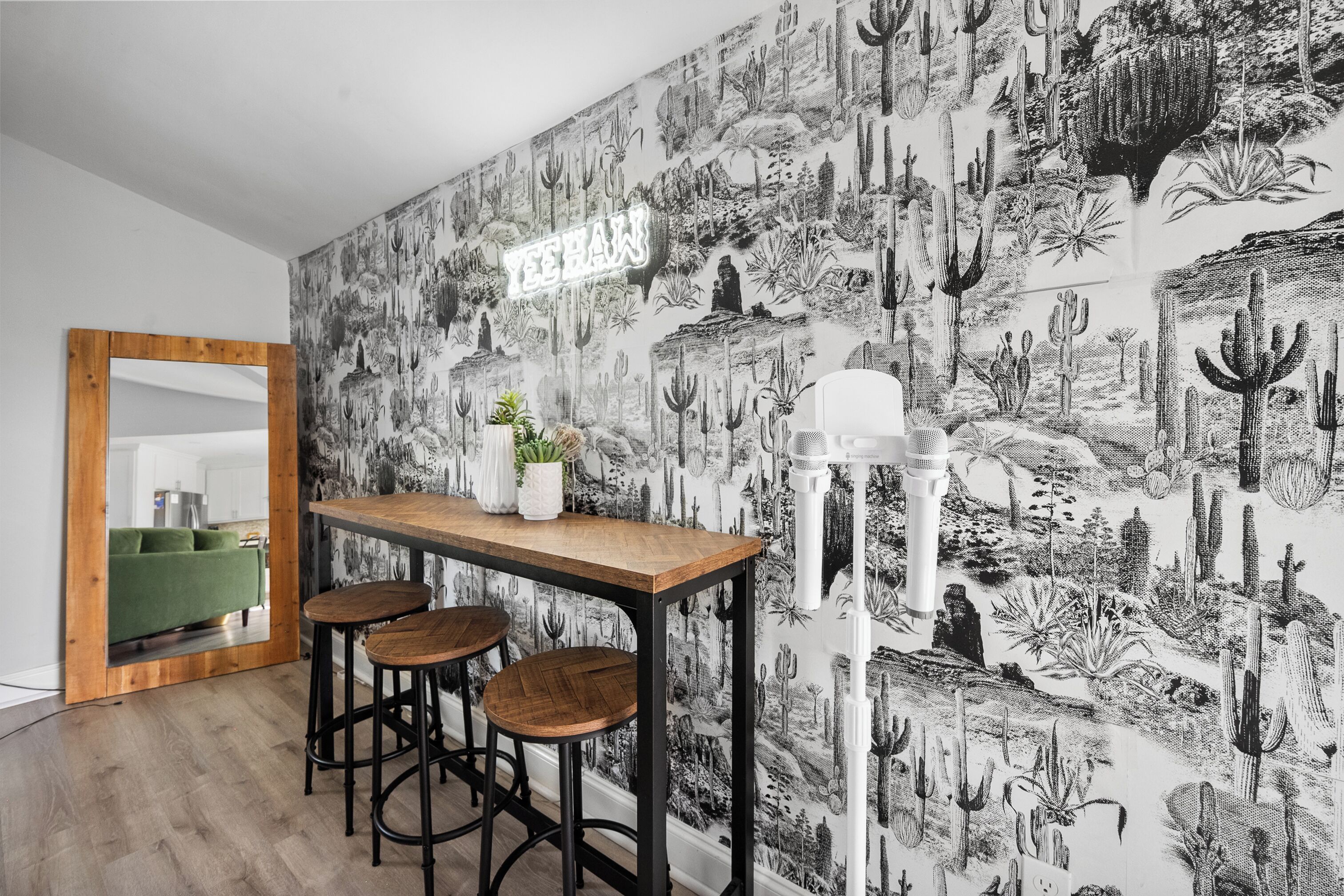 A room with a cactus-themed wallpaper, a wooden table with stools, and a mirror on the wall.