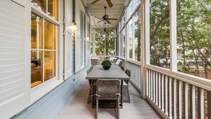 Une véranda abritée avec une table et des chaises, des ventilateurs de plafond et de grandes fenêtres.