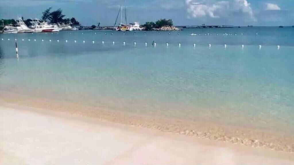 Ein Strand mit klarem Wasser, Booten und einer entfernten Insel.