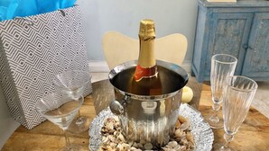 A table with a champagne bottle in a metal bucket, surrounded by seashells, two empty wine glasses, and a gift bag. - Beachside Tropics - King Bed (Ocho Rios)