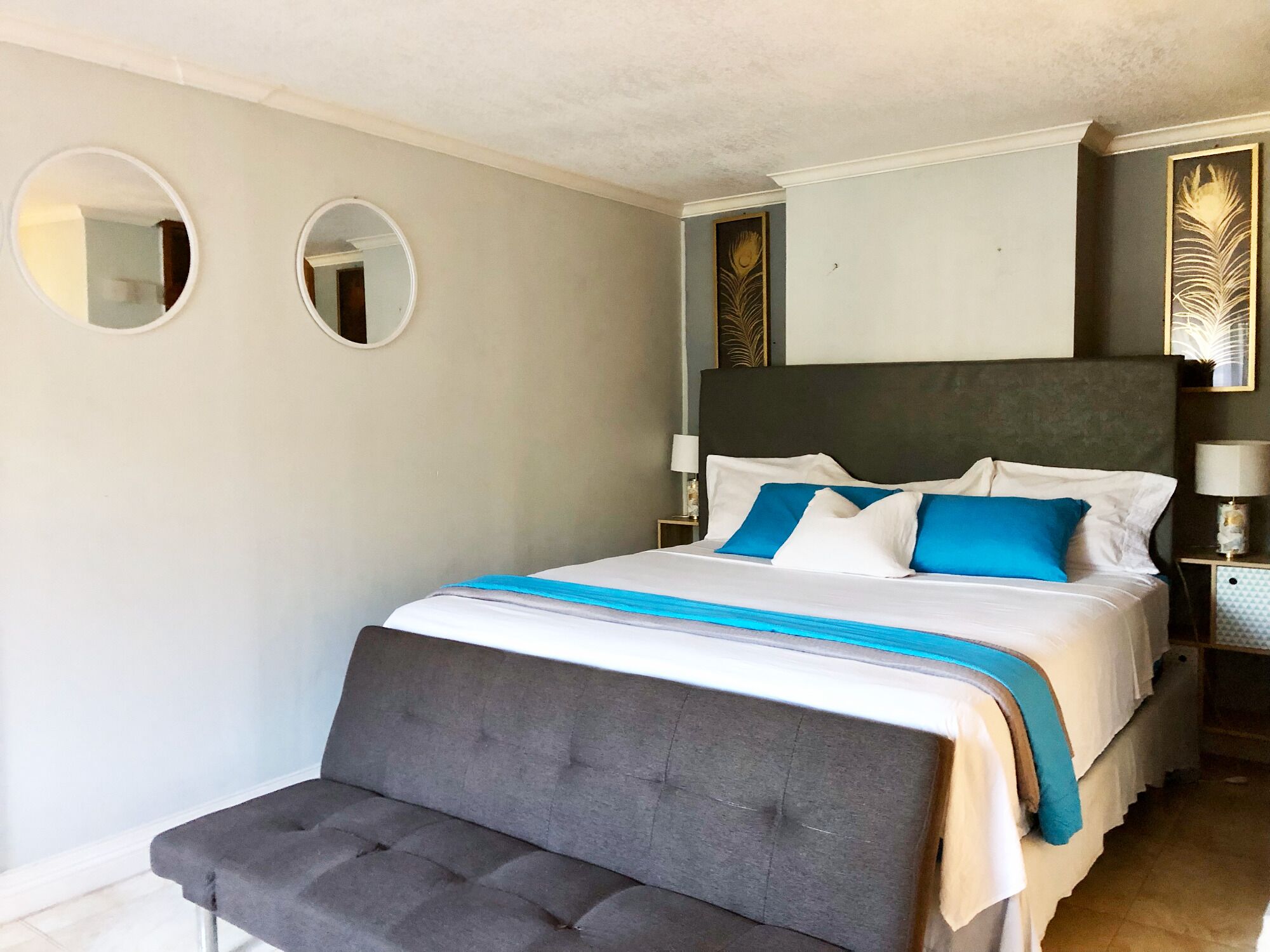 Ein ordentlich eingerichtetes Schlafzimmer mit einem großen Bett, zwei Nachttischen und zwei an der Wand befestigten Spiegeln.