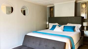 Ein ordentlich eingerichtetes Schlafzimmer mit einem großen Bett, zwei Nachttischen und zwei an der Wand befestigten Spiegeln.