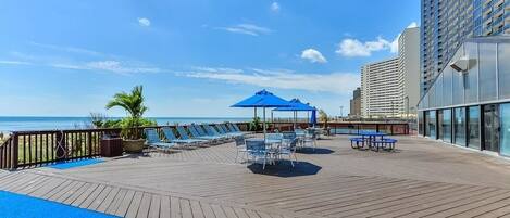 A wooden deck with lounge chairs and umbrellas, overlooking a beach and ocean.