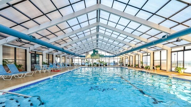Une piscine intérieure à l’eau d’un bleu limpide, entourée de chaises longues et de plantes en pot.