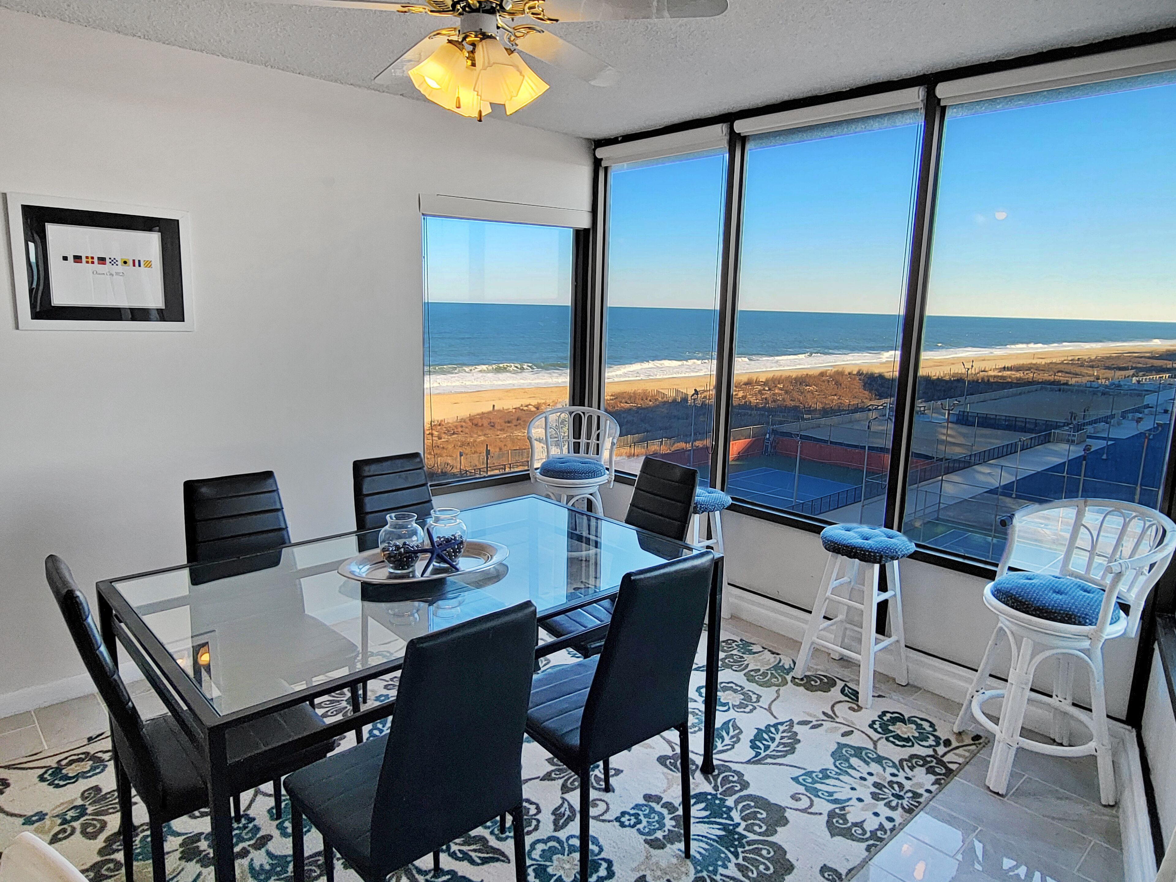 Ein modernes Zimmer mit Glastisch, schwarz-weißen Stühlen und einem großen Fenster mit Blick auf Strand und Meer.