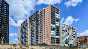 Un immeuble résidentiel de grande hauteur, doté de nombreux balcons, situé à proximité d’une plage de sable.