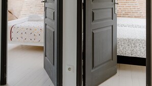 Een kamer met een schuine plafond, een bed met een bedovertrek met patroon, en een bakstenen muur op de achtergrond.