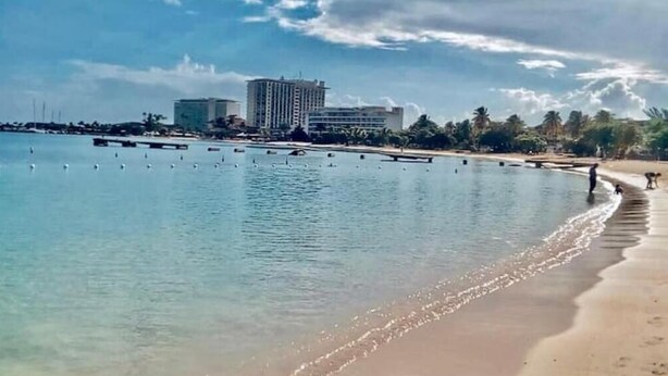 A beach with clear water, a sandy shore, and buildings in the background. - Beachfront Escape (Ocho Rios)