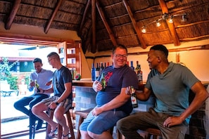 A group of people seated at a bar with a thatched roof, holding bottles of drinks.