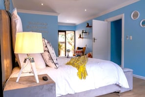A bedroom with a bed, a lamp, a quote on the wall, and a view of the outdoors.