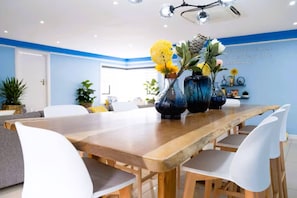 A modern dining area with a long wooden table, white chairs, and decorative vases with flowers.