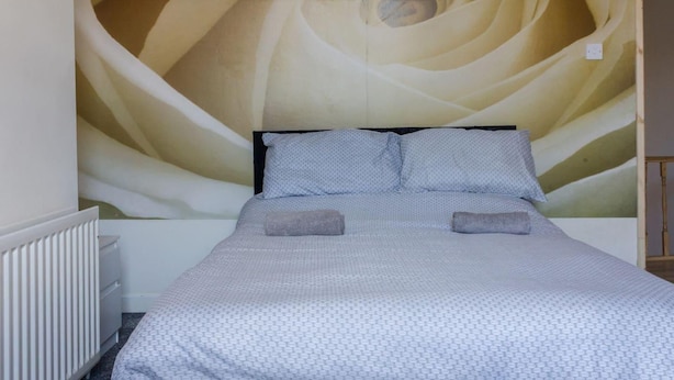 A bedroom with a large wall mural, a bed with a patterned bedspread, two pillows, and a bedside table.
