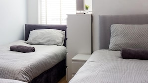 A hotel room with two beds, each with a headboard, a bedside table, and a lamp.