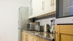 A kitchen with white cabinets, a refrigerator, a microwave, a toaster, and a kettle.