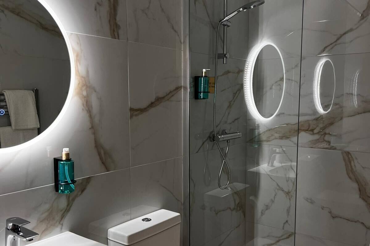 A modern bathroom with a glass-enclosed shower, a round mirror, and a toilet.