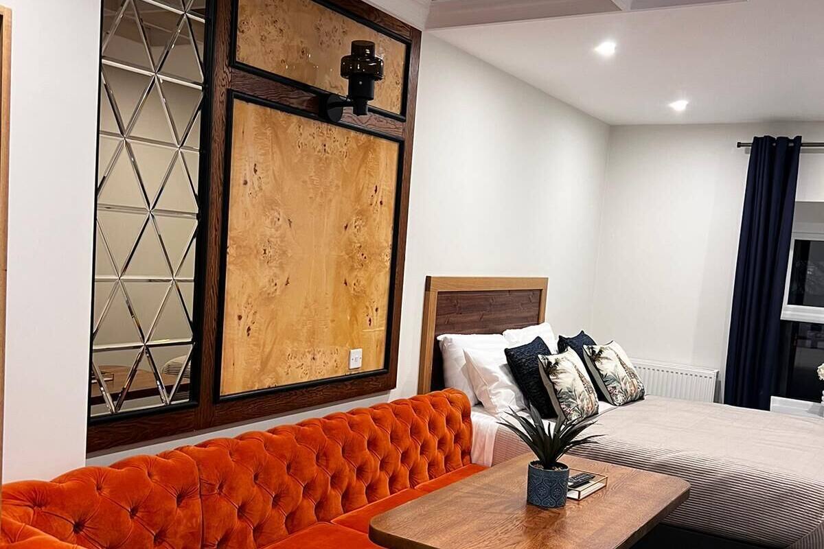 A modern hotel room with a tufted orange sofa, a wooden coffee table, and a bed with a headboard.