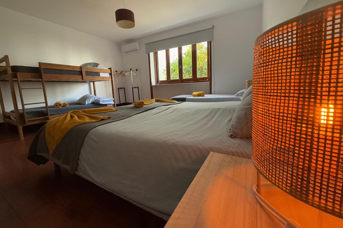 Ein Zimmer mit Etagenbetten, einem Fenster mit Blick auf Grünflächen und einer Lampe mit gemustertem Lampenschirm.