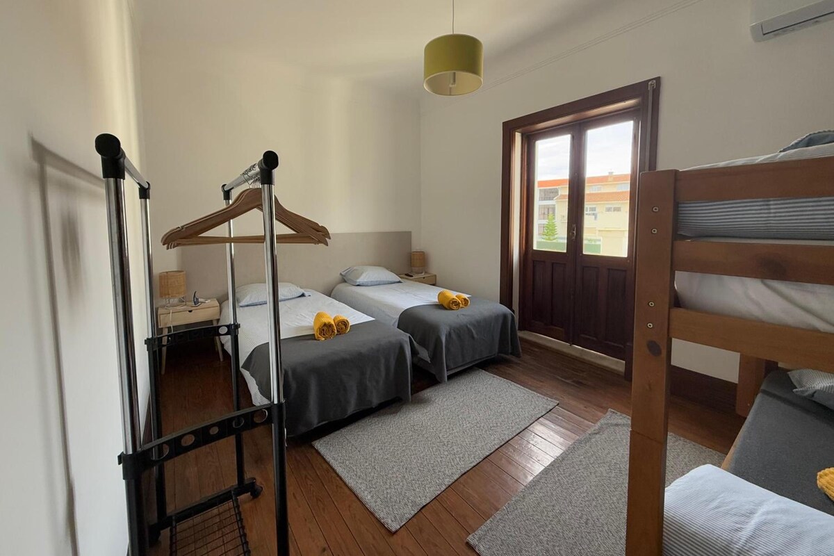 A room with two beds, a hanging chair, a wooden bunk bed, and a window with a view.