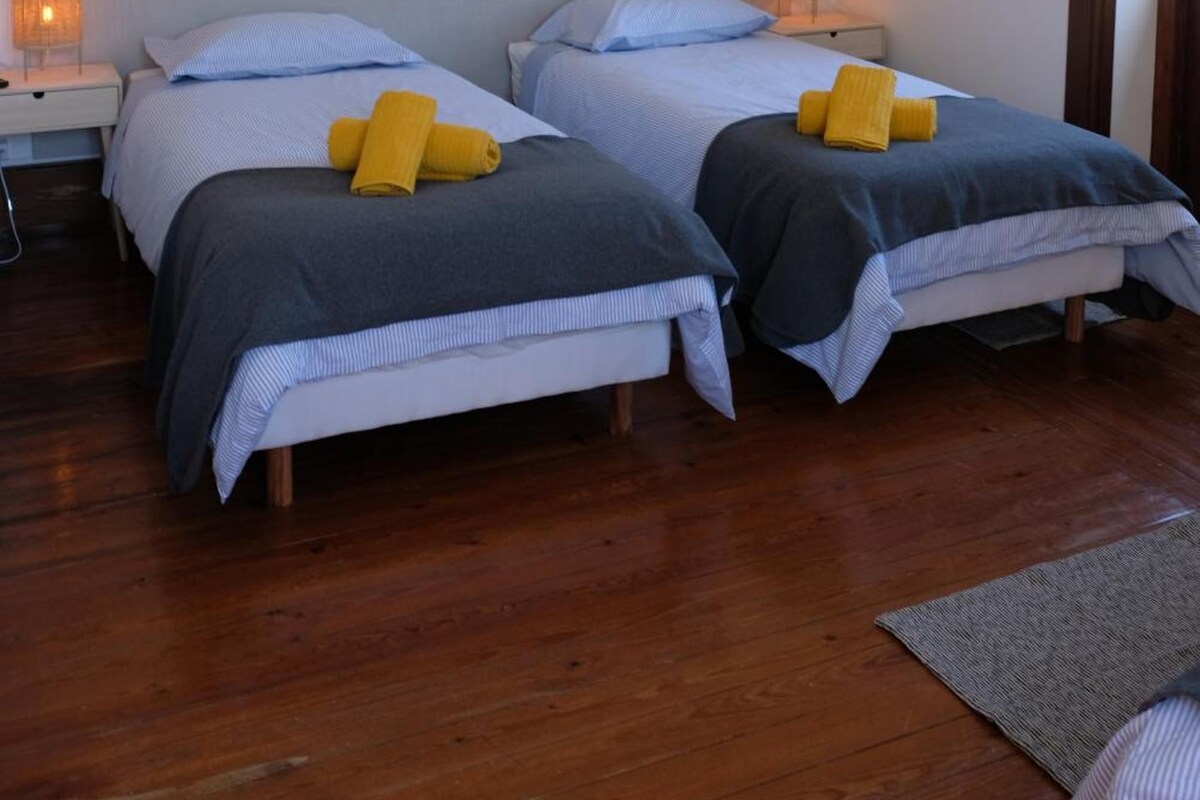 Ein Zimmer mit zwei Betten, jeweils mit Kopfstütze, Nachttisch und Lampe.