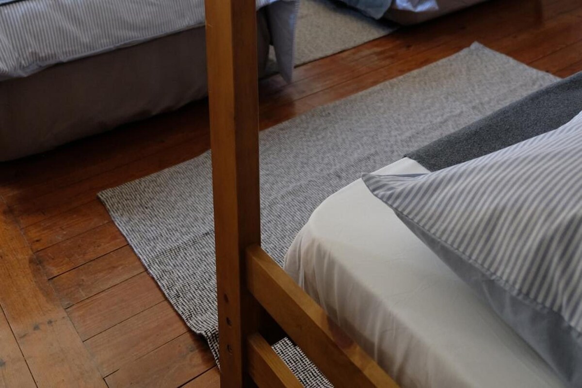 Habitación con literas, dos camas, una mesita de noche y piso de madera.