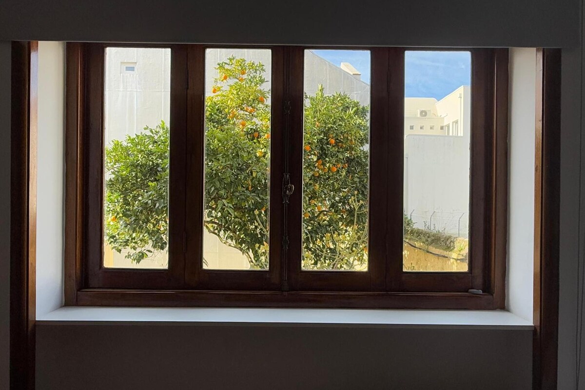 A window with a view of a tree with orange fruits, a white building, and a clear sky.
