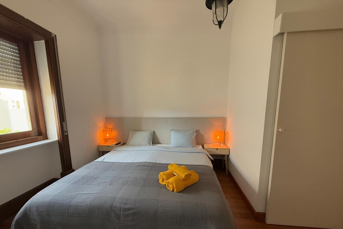 A hotel room with a bed, two bedside tables with lamps, a window, and a door.