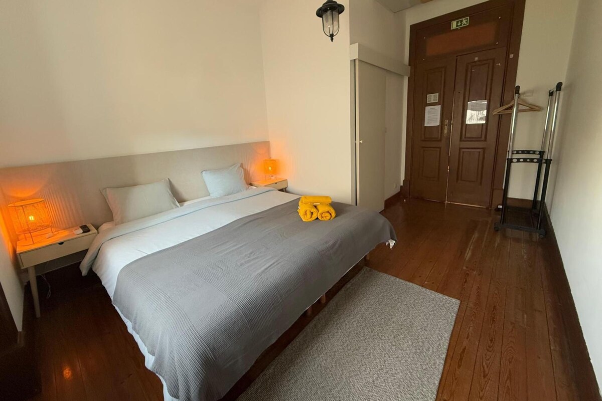 Habitación de hotel con cama, lámparas de noche, piso de madera y una puerta con letrero de salida.