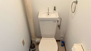 Un baño pequeño y funcional con inodoro blanco, lavamanos pequeño y dispensador de papel higiénico.