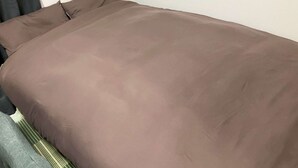 Una cama con una colcha marrón y almohadas, una funda de almohada a rayas y una manta verde a rayas.