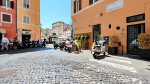 A cobblestone street lined with parked scooters and motorcycles, buildings with signage, and a clear blue sky. - House of Mamas (Rome)