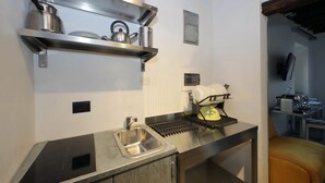 A compact kitchen with a stainless steel sink, a kettle, and a dish rack. - House of Mamas (Rome)