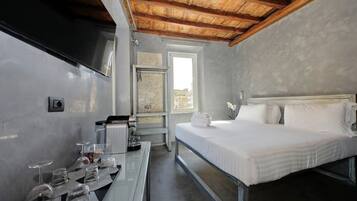 Une chambre d’hôtel avec un lit, une table avec des verres et une bouilloire, une fenêtre et une vue sur les bâtiments environnants.