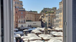 A bustling outdoor market with numerous white umbrellas, a clock tower, and historic buildings. - House of Mamas (Rome)