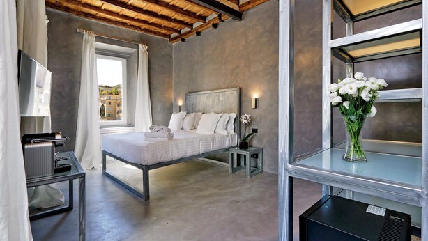 A bedroom with a bed, bedside tables, a mirror, a window with curtains, and a view of buildings outside. - House of Mamas (Rome)