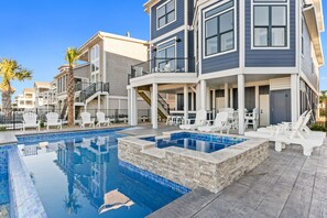 A modern residential building with a swimming pool, outdoor seating, and a covered patio area. - Oasis Vacations, Old Man By The Sea. Infinity Pool, Elevator, Marsh Views! (Ocean Isle Beach)