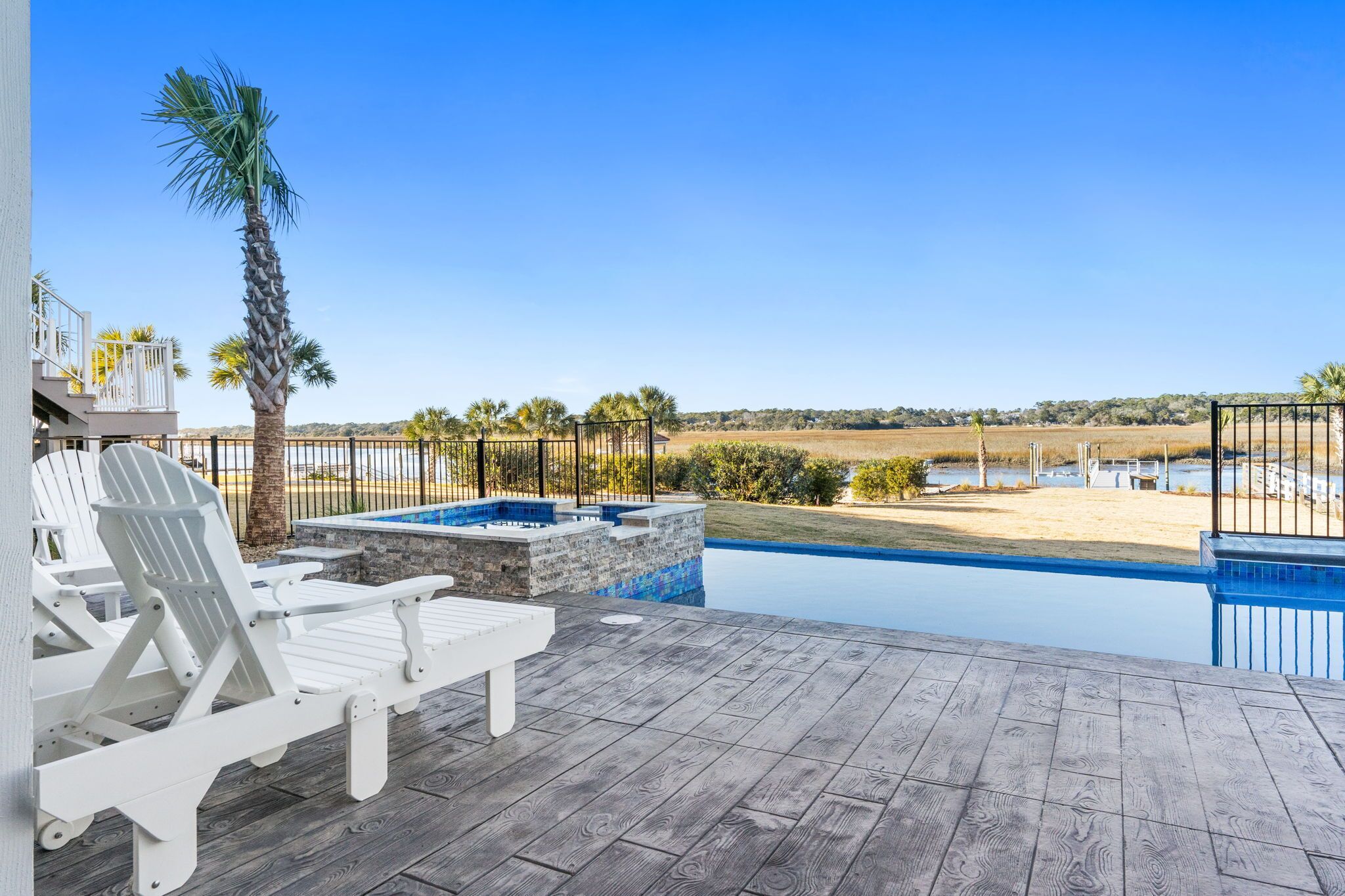 Une terrasse en bois avec une piscine, des chaises longues blanches et une vue sur une plage et des champs.