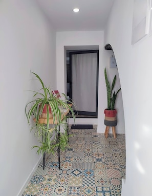 A hallway with patterned floor tiles, a potted plant, and a door with a curtain. - Character 2BR Upper Retreat With BBQ Terrace Parking (Ponta Delgada)