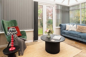 A room with a green armchair, a blue sofa, a black coffee table, and a window with blinds.