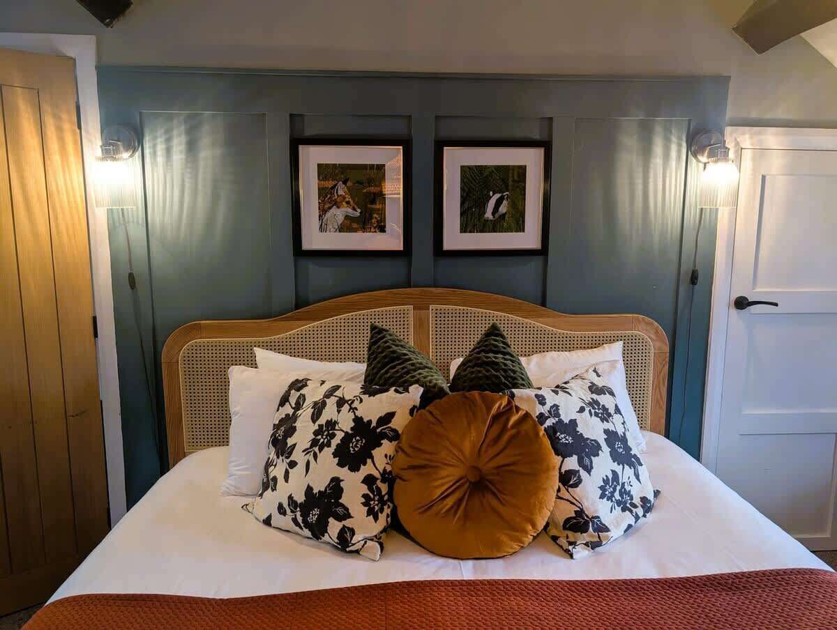 Un lit avec une tête de lit en bois, plusieurs oreillers et deux tableaux encadrés accrochés au mur au-dessus.