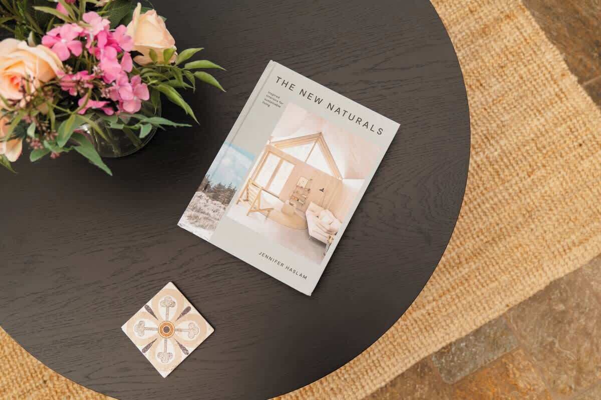 Un libro titulado 'The New Naturals' de Jennifer Kaslam sobre una mesa redonda con una planta en maceta y un adorno.