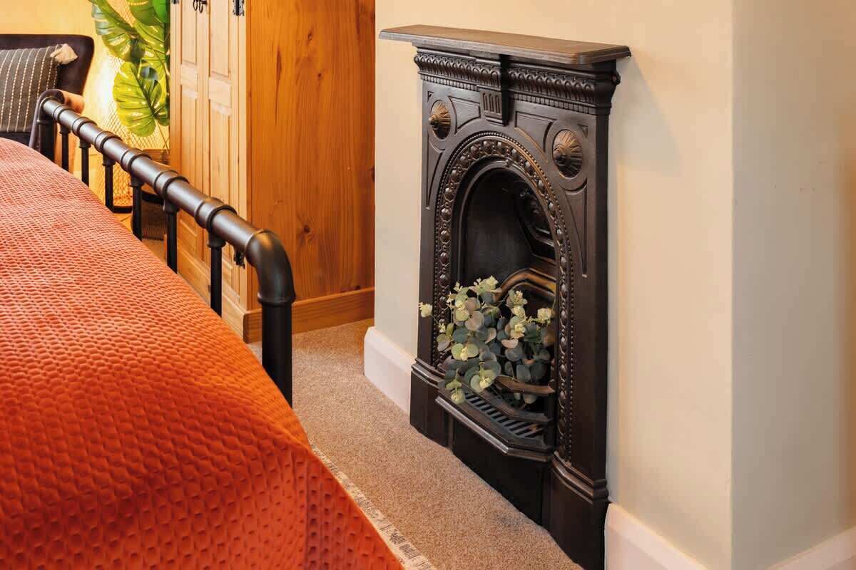 Een kamer met een bed, een houten garderobe en een open haard met decoratieve details.