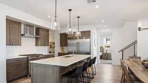 Una cocina moderna con una isla grande, electrodomésticos de acero inoxidable e iluminación colgante.