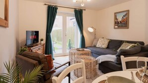 A living room with a sofa, a TV, a dining table with chairs, and a window with curtains. - Stylish Chester Stay, Free Parking, Private Garden (Cheshire West and Chester)