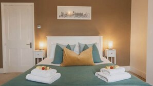A neatly made bed with a green bedspread, two white towels, and a cityscape picture on the wall. - Park and walk to city centre!  Cosy terrace (Handbridge)
