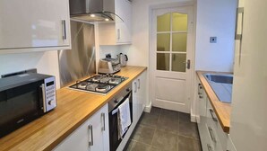 A compact kitchen with a microwave, gas stove, and a window with frosted glass. - Park and walk to city centre!  Cosy terrace (Handbridge)