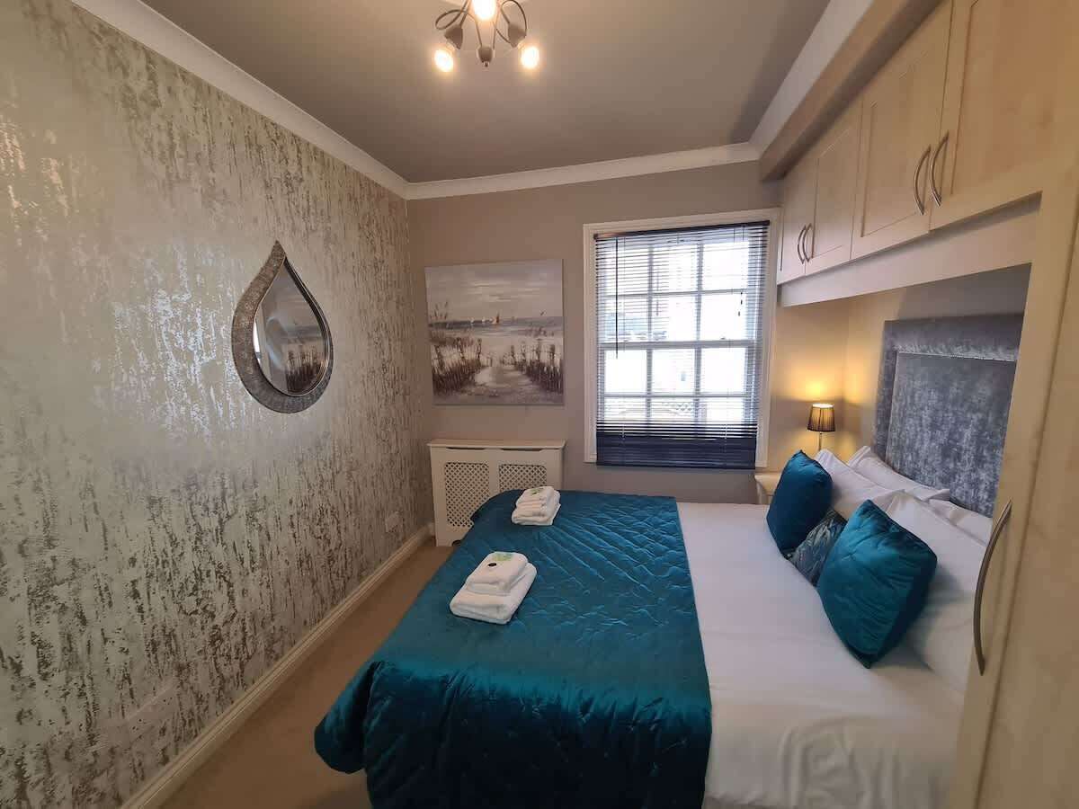Un dormitorio con cama, una ventana con persianas, un espejo montado en la pared y un cuadro.