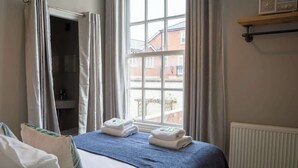 A hotel room with a bed, a window with curtains, a radiator, and a shelf with towels. - 2 Bed - City Centre on your doorstep Parking! (Cheshire West and Chester)