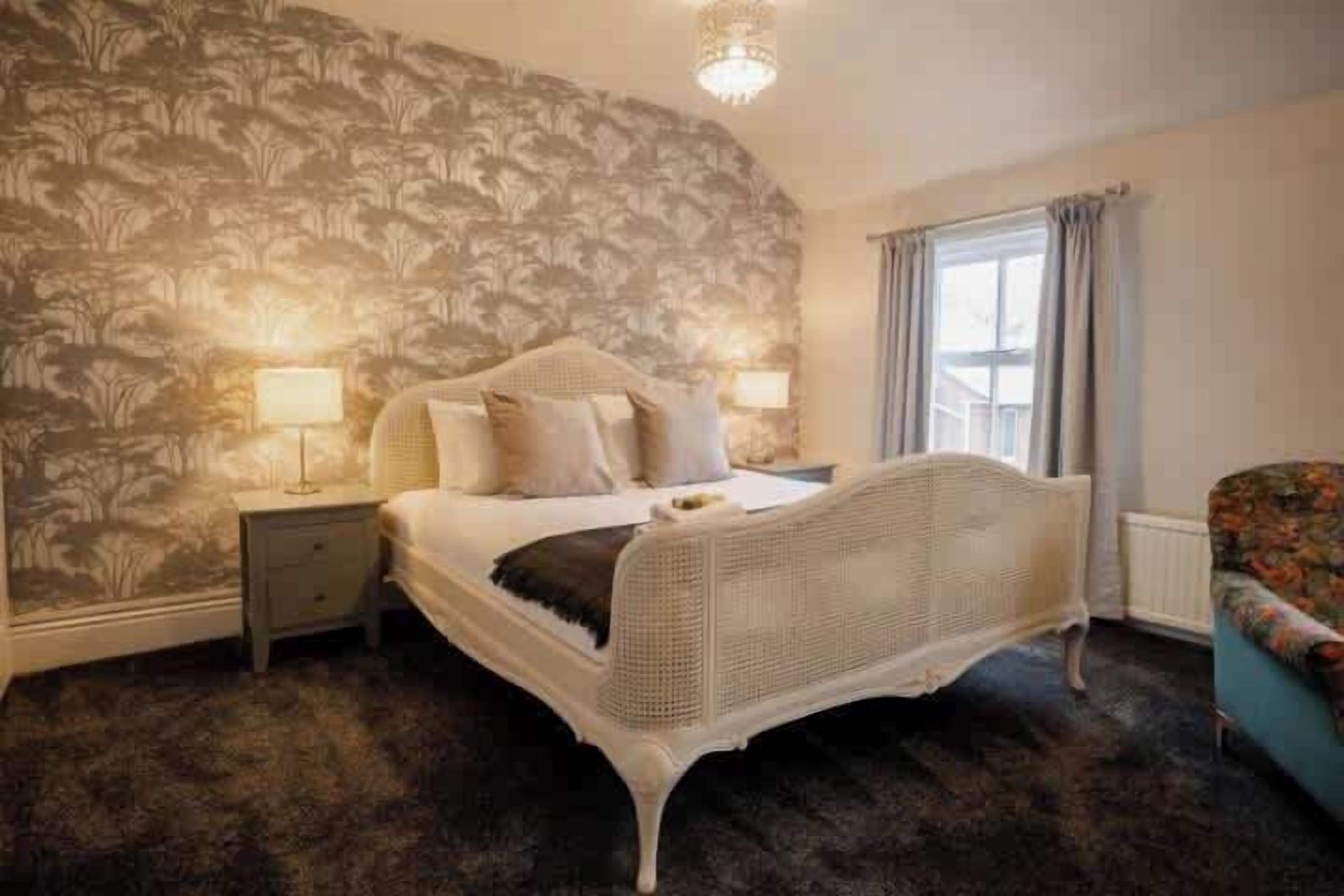 Een slaapkamer met een groot bed, twee nachtkastjes, een raam met gordijnen en een wand met bloemenmotief.