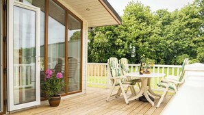 A wooden deck with a table and chairs, a potted plant, and a glass door leading to a room. - Cosy Lodge on Farm with Donkeys, Parking (Chester)