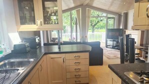 A kitchen with a sink, stove, and cabinets. There is a television and a seating area with a view of the outdoors. - Cosy Lodge on Farm with Donkeys, Parking (Chester)